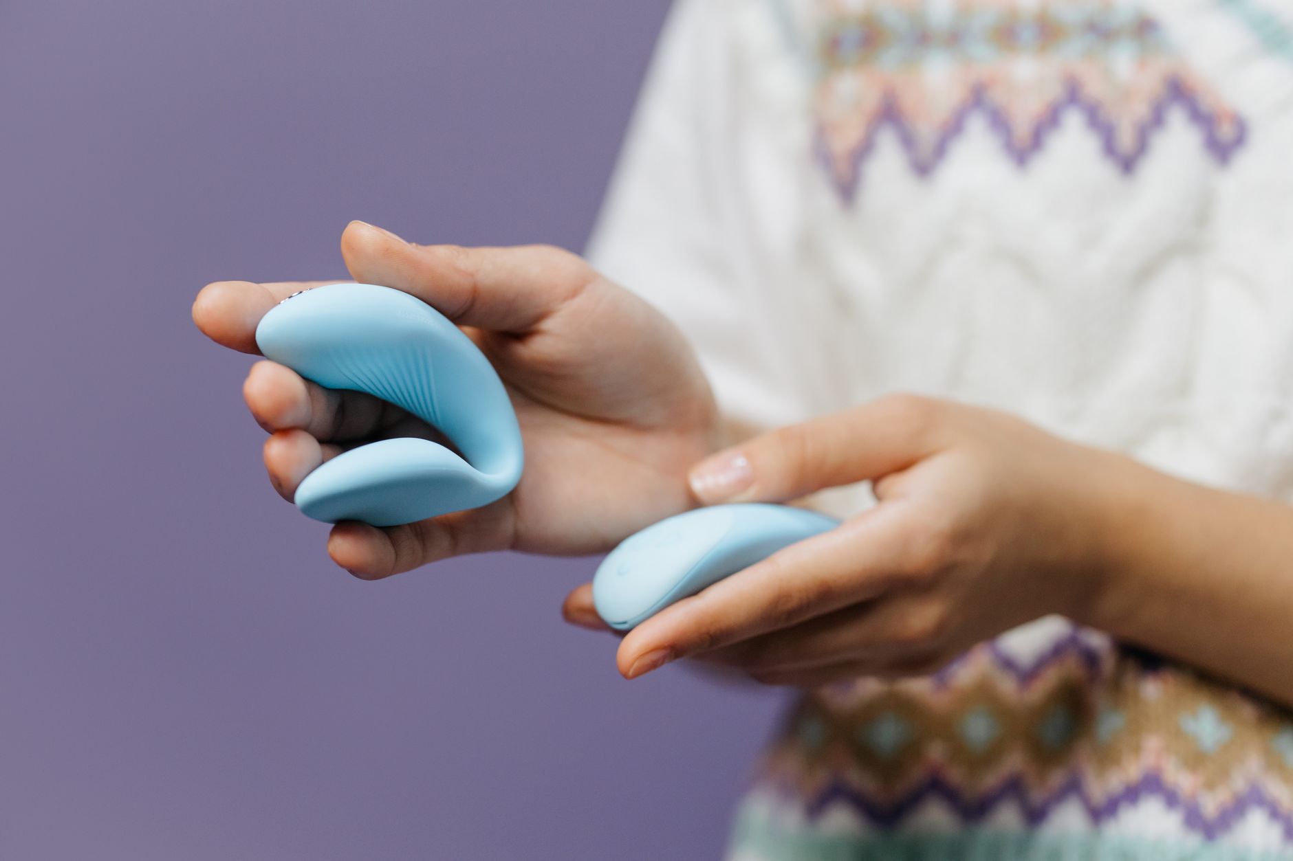 Close-up of hands holding a sleek blue clitoral vibrator against a purple background