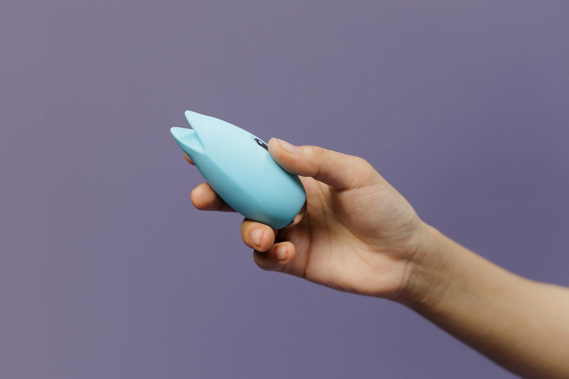 Vibrador de silicone azul segurado em mão contra fundo roxo sólido, promovendo amor próprio e sexualidade