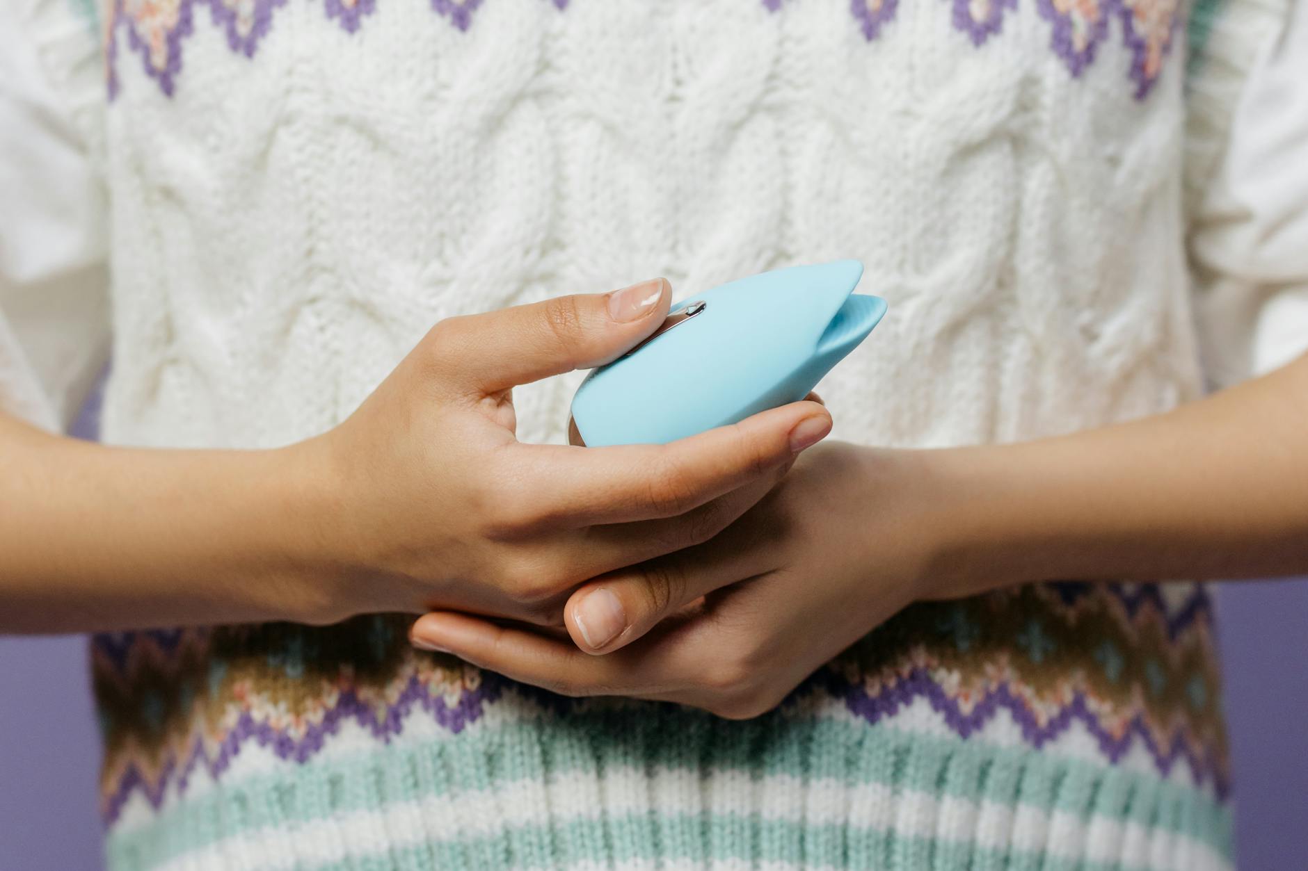 Mãos segurando um vibrador azul contra uma blusa de malha, representando exploração sensual cuidadosa