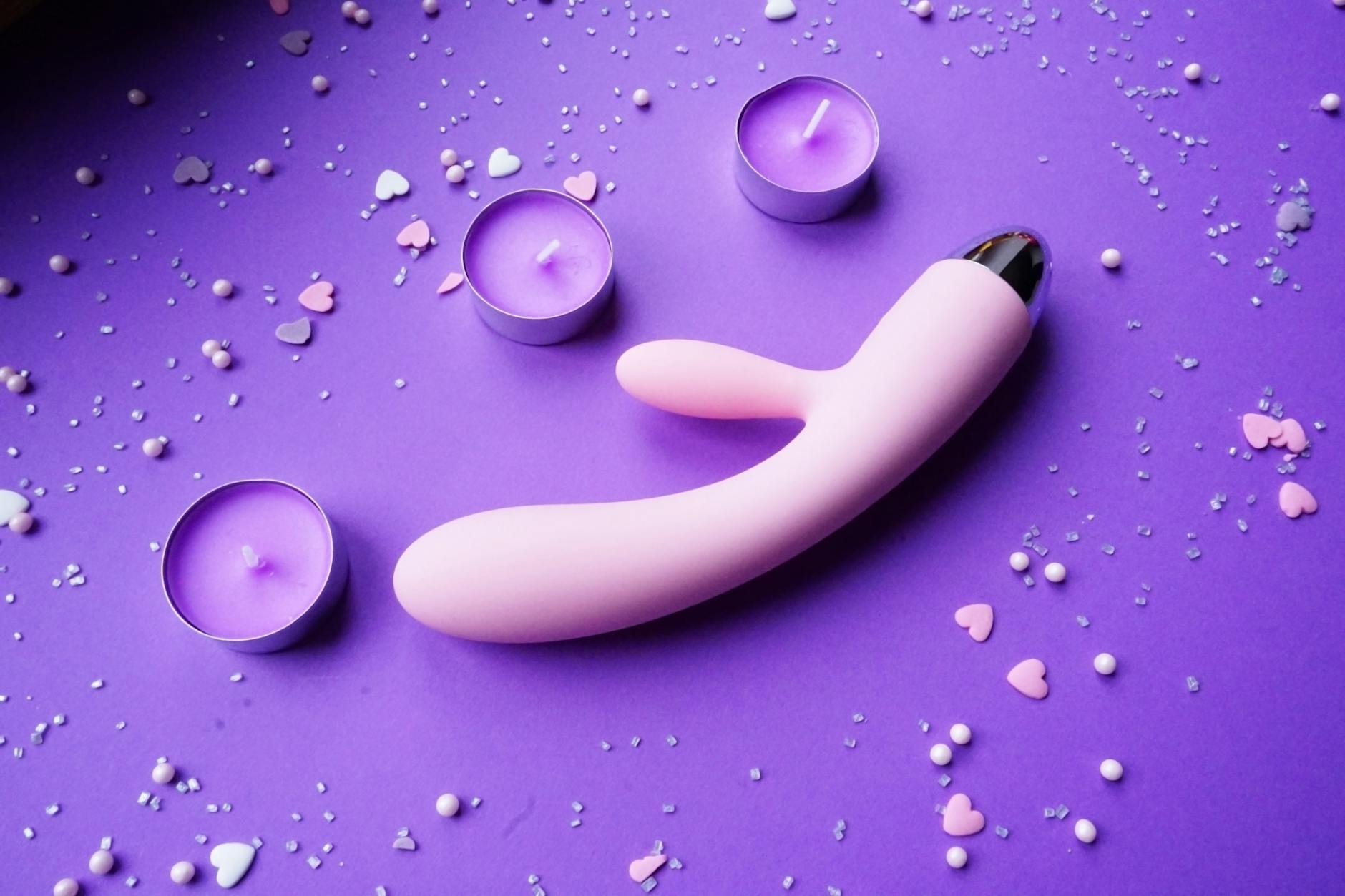 Vibrador rosa em fundo roxo com confetes de coração e velas para clima romântico